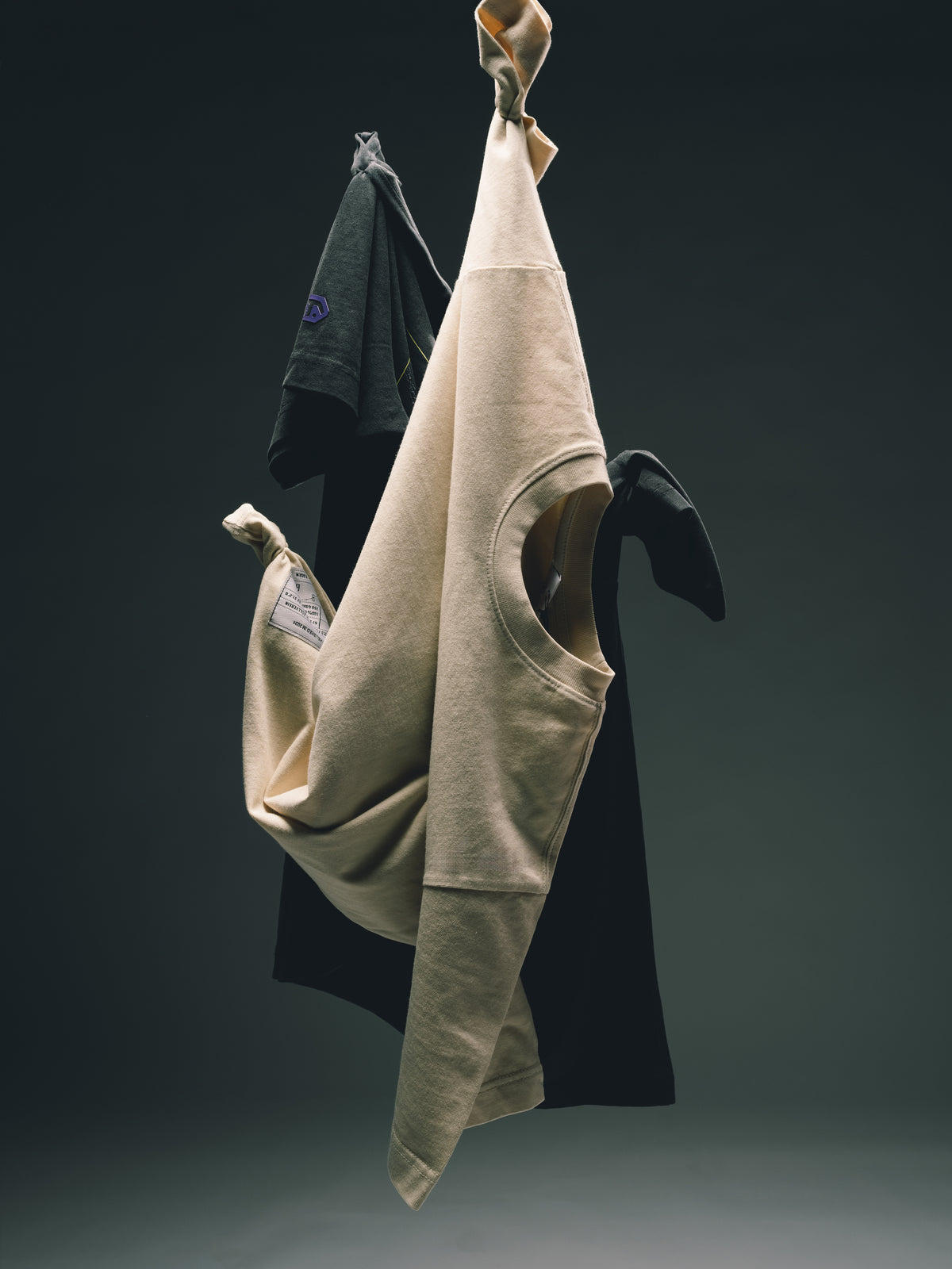 Beige und schwarze Kleidungsstücke kunstvoll an den Ärmeln aufgehängt und frei vor einem dunkelgrauen Hintergrund schwebend.